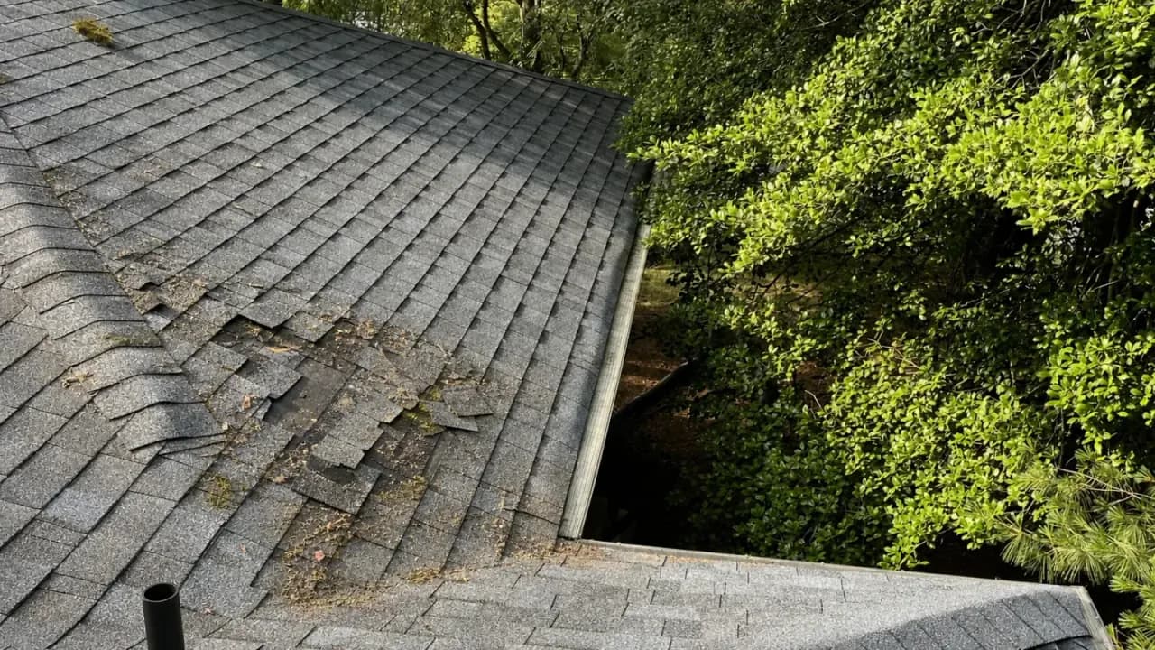 Photo of a residential roof with cracked, curling, and missing asphalt shingles exposing the wood decking underneath
