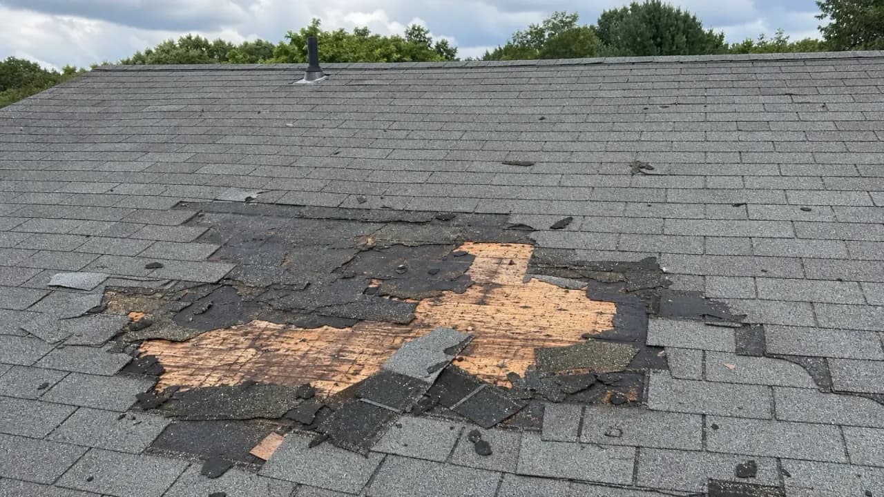 Photo of a residential roofline near the gutter edge with storm-damaged, curled, and missing shingles